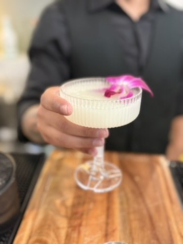 A frothy cocktail in a ribbed coupe garnished with an orchid